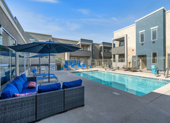a pool with lounge chairs and umbrellas at the whispering winds apartments in pearland, at Loma Villas Apartments, San Bernardino, 92408