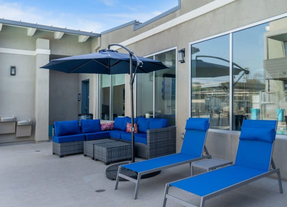 a patio with blue lounge chairs and a blue umbrella at Loma Villas Apartments, California