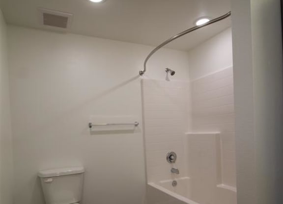 a white toilet sitting next to a bath tub at Loma Villas Apartments, San Bernardino