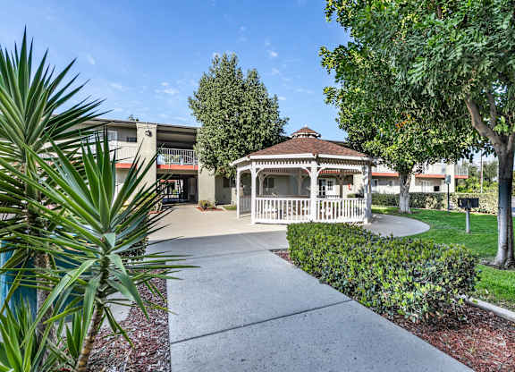 A gazebo is surrounded by a small garden and a concrete walkway. at Canyon Shadows Apartments, Riverside, CA  