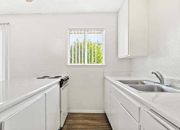 A kitchen with white cabinets and a window with a view of trees. at Canyon Shadows Apartments, Riverside