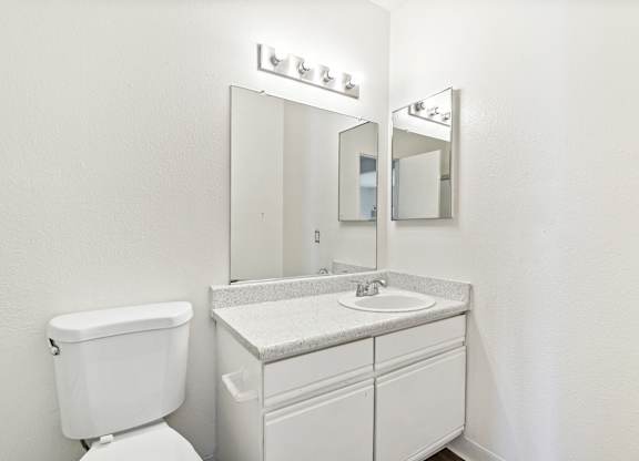 A white bathroom with a toilet, sink, and mirror. at Canyon Shadows Apartments, Riverside, CA