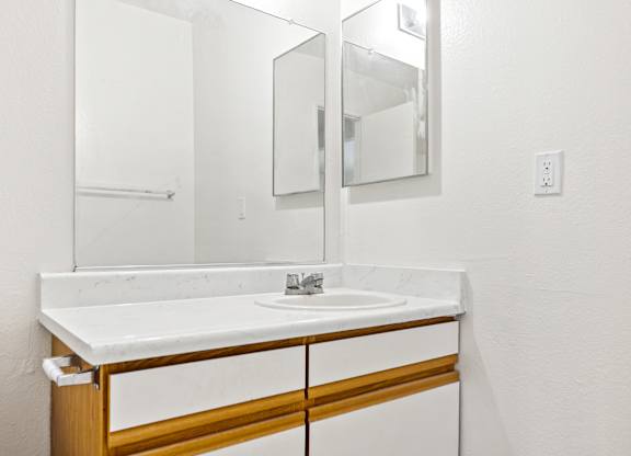 A white sink with a wooden frame and a mirror above it. at Canyon Shadows Apartments, Riverside, CA 92503  