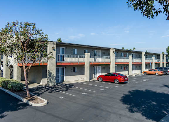 A red car is parked in a parking lot in front of a building at Canyon Shadows Apartments, California, 92503.