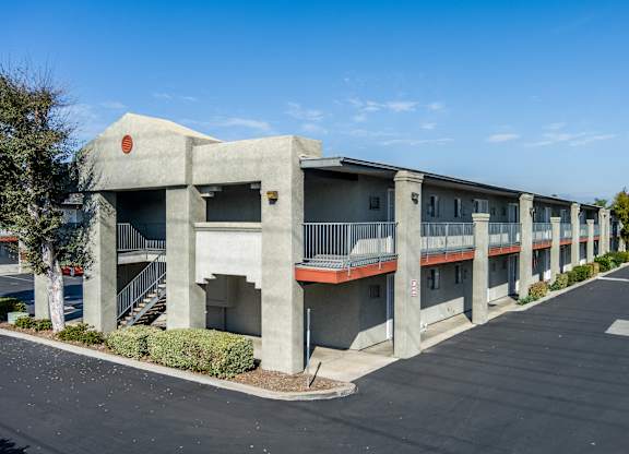 A concrete building with a red roof and a parking lot in front. at Canyon Shadows Apartments, Riverside