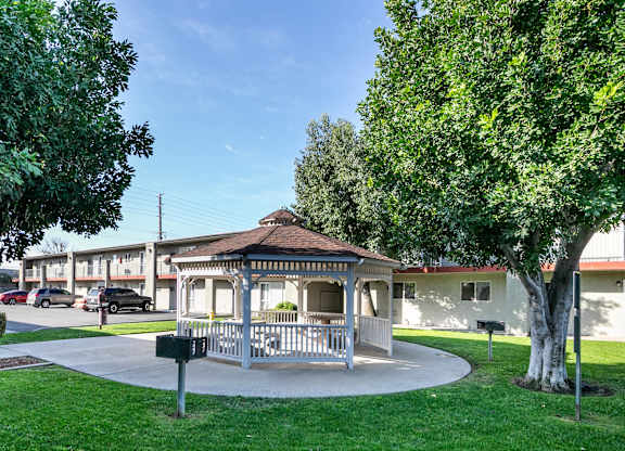 A gazebo is in the middle of a grassy area in front of a building. at Canyon Shadows Apartments, Riverside, CA 92503  