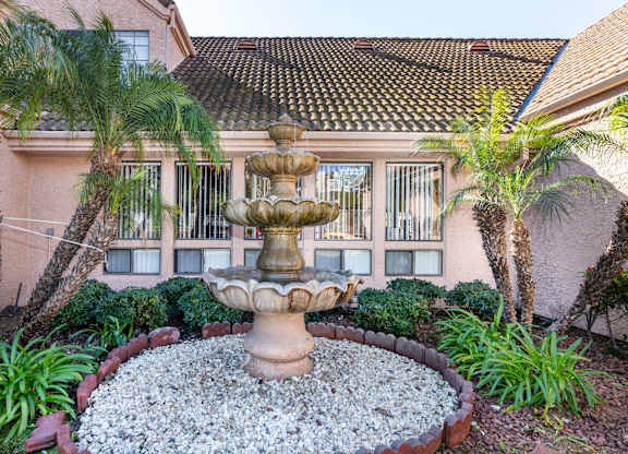 A fountain in the middle of a garden with a building in the background. at Whispering Fountains Diamond Bar, Diamond Bar, CA 91765