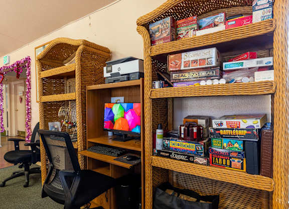 A room with a computer desk and a shelf with board games. at Whispering Fountains Diamond Bar, Diamond Bar