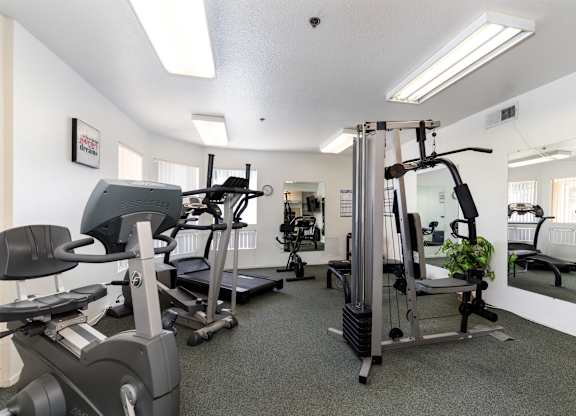 A gym with a variety of equipment including treadmills, elliptical machines, and a weight machine. at Whispering Fountains Diamond Bar, California