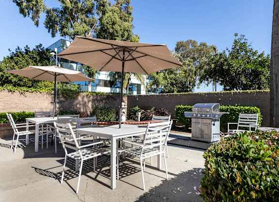 A patio with a table and chairs under an umbrella. at Whispering Fountains Lakewood, California, 90805