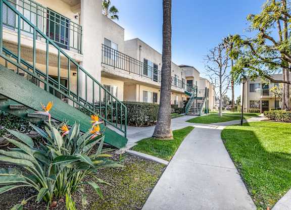 A pathway leads through a grassy area between two rows of apartment buildings. at Whispering Fountains Lakewood, Lakewood Bar