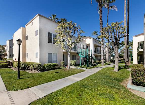 A row of houses with a sidewalk and green grass. at Whispering Fountains Lakewood, Lakewood Bar California