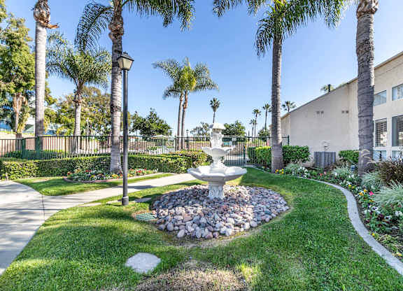 A garden with a fountain surrounded by palm trees. at Whispering Fountains Lakewood, Lakewood Bar, 90805