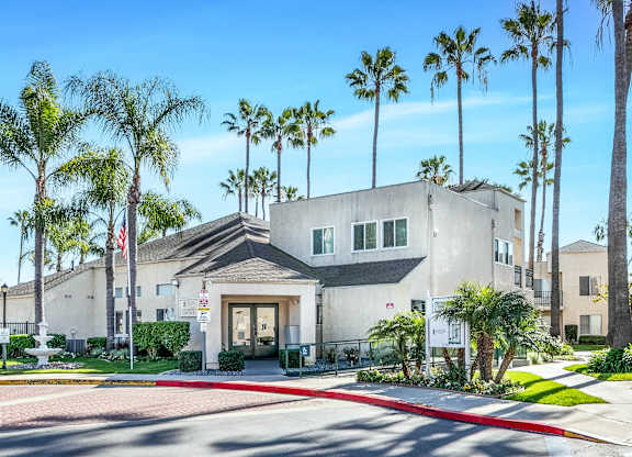 A building with a flag in front of it and palm trees around. at Whispering Fountains Lakewood, Lakewood Bar, CA 90805