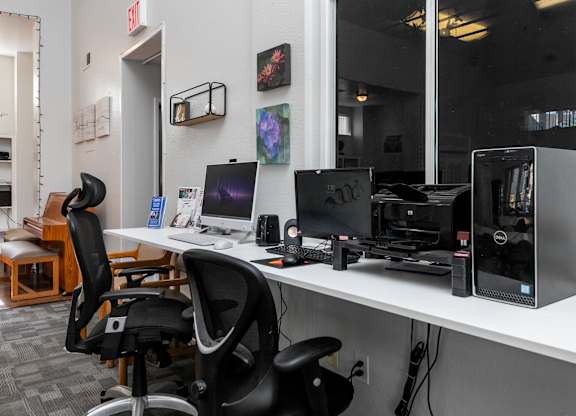 A black chair is in front of a desk with a computer and a monitor. at Whispering Fountains Lakewood, California