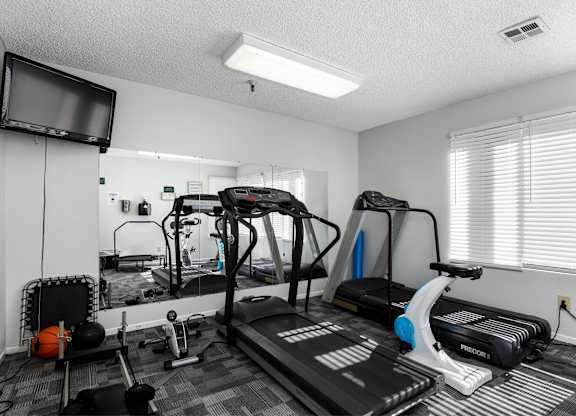 A home gym with a treadmill, exercise bike, and other equipment. at Whispering Fountains Lakewood, California