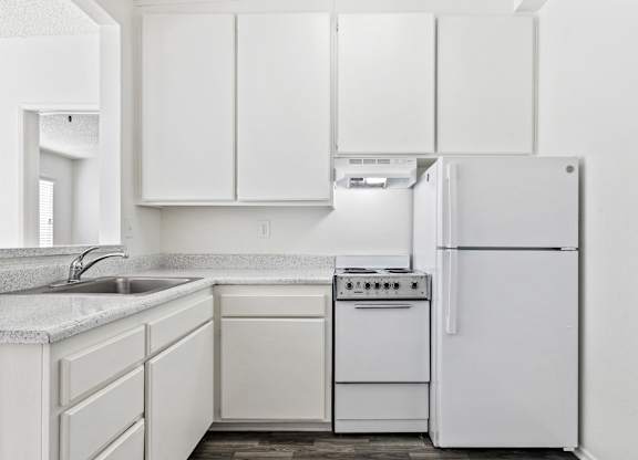 A white kitchen with a refrigerator, sink, and cabinets. at Whispering Fountains Lakewood, Lakewood Bar California