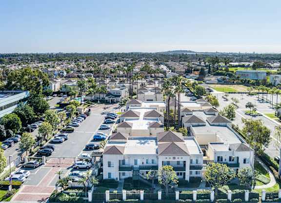 A large white building with a red roof is surrounded by a parking lot. at Whispering Fountains Lakewood, Lakewood Bar, 90805