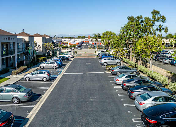 A parking lot with cars parked in rows and apartment buildings in the background. at Whispering Fountains Lakewood, Lakewood Bar, CA 90805