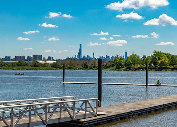 A dock extends into a calm body of water with a city skyline in the distance at Vermella Lyndhurst apartments, New Jersey, 07071
