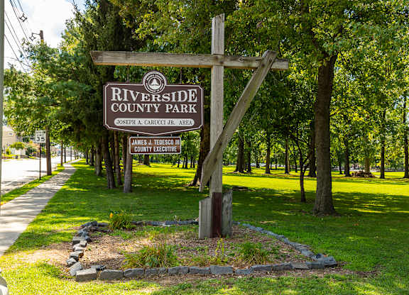 A sign for Riverside County Park is displayed in front of a wooded area at Vermella Lyndhurst apartments, Lyndhurst