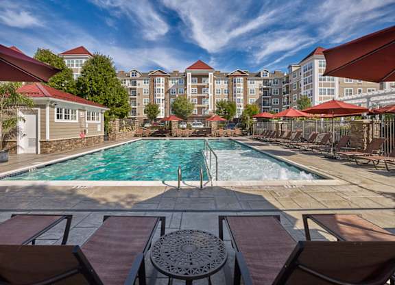 A pool surrounded by chairs and umbrellas with apartment buildings in the background at Vermella Lyndhurst apartments, Lyndhurst, New Jersey