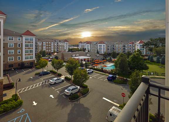 A sunset view of a parking lot with cars parked and a pool in the distance at Vermella Lyndhurst apartments, Lyndhurst, New Jersey