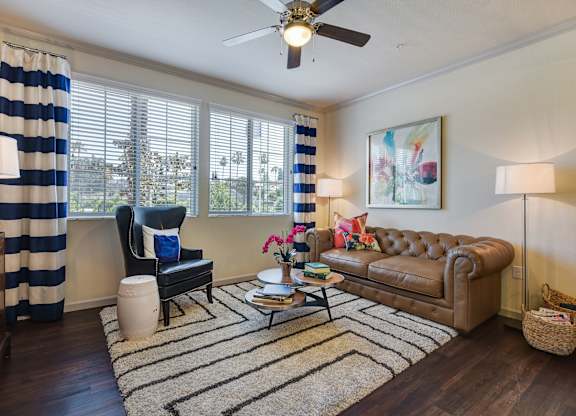 A living room with a brown leather couch, a black chair, and a striped curtain.