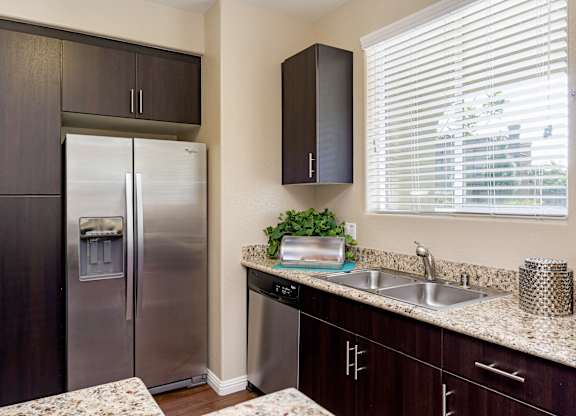 A kitchen with a stainless steel refrigerator and dark brown cabinets.