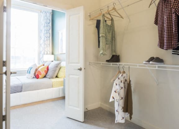 a closet with clothes hanging on a rack and a door to a bedroom