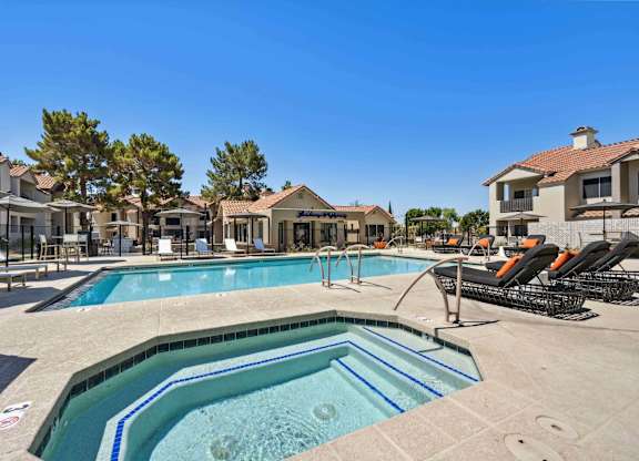 A large outdoor swimming pool surrounded by lounge chairs and buildings.