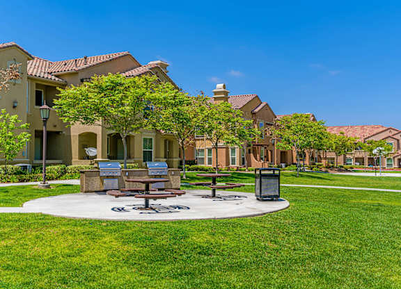 A sunny day at a park with benches and a trash bin.