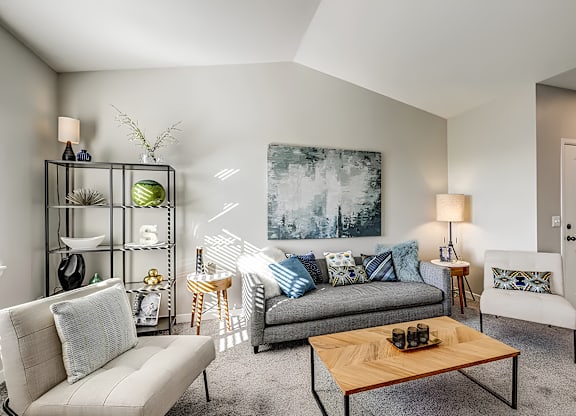 A living room with a grey couch, a wooden coffee table, and a grey and white patterned armchair.