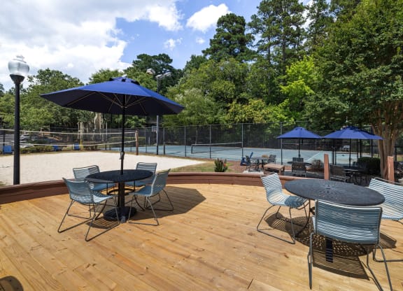 a patio with tables, blue umbrellas with the swimming pool in the background