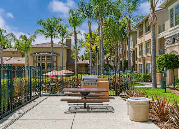 A park area with a picnic table and benches in front of a gated community.