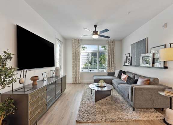 A living room with a grey couch, a black television, and a ceiling fan.
