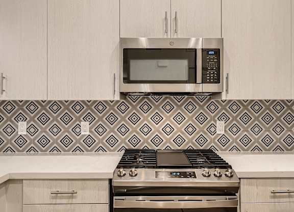 A modern kitchen with a stove, microwave, and patterned backsplash.