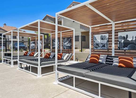 A row of white and grey outdoor beds with orange cushions.