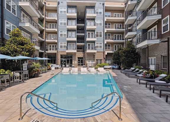 an outdoor swimming pool with lounge chairs and umbrellas in front of an apartment building