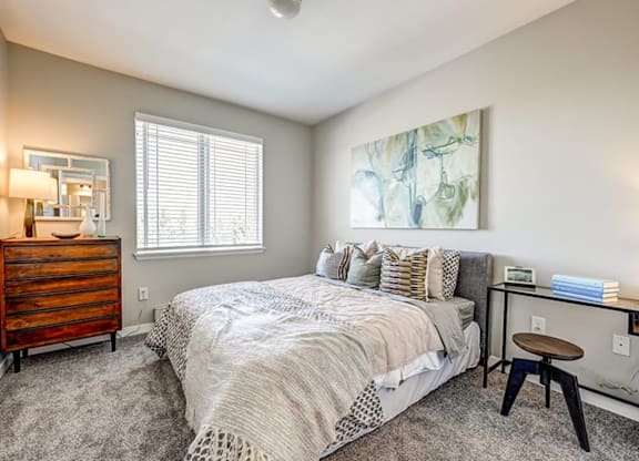 A bedroom with a bed, nightstand, and a painting on the wall.