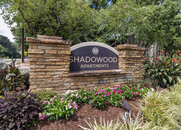 the shadwood apartments sign on a stone wall with plants