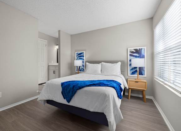 A bedroom with a bed, nightstand, and a window with blinds.