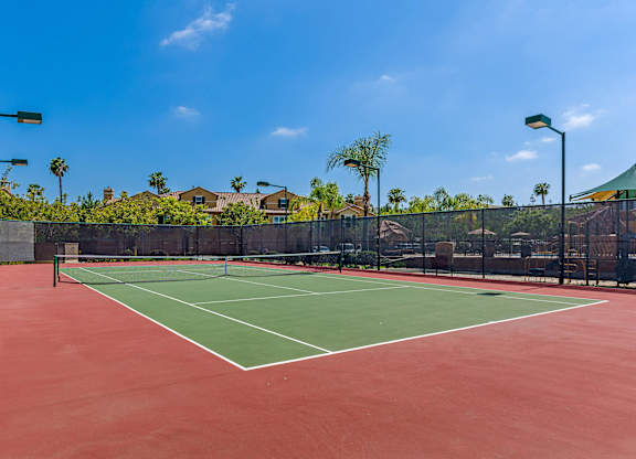 A tennis court with a red surface and green boundary lines.