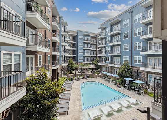 an outdoor pool with lounge chairs and umbrellas in front of an apartment building