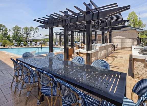 A black table with blue chairs is set up by a pool.