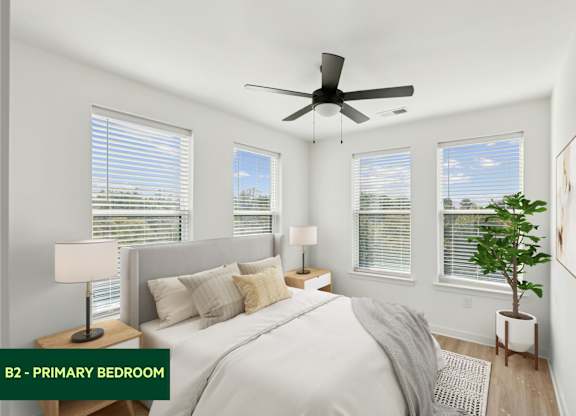 A bedroom with a bed, two lamps, a ceiling fan, and a potted plant.
