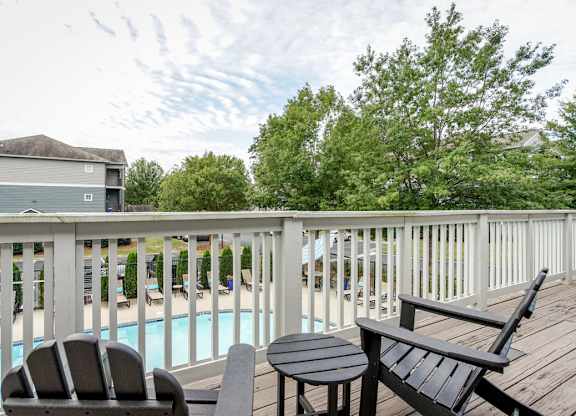 A wooden deck with a table and two chairs overlooking a pool.