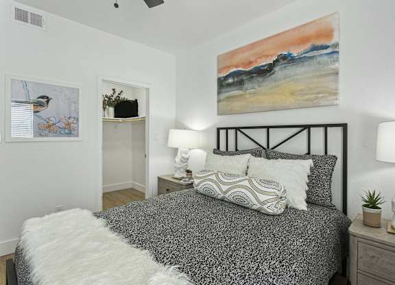 A bedroom with a bed, two lamps, and a painting on the wall.