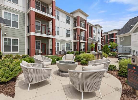 A patio with white chairs and a table is in front of apartment buildings.