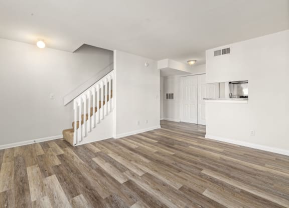 the living room and kitchen of a house with white walls and wood floors